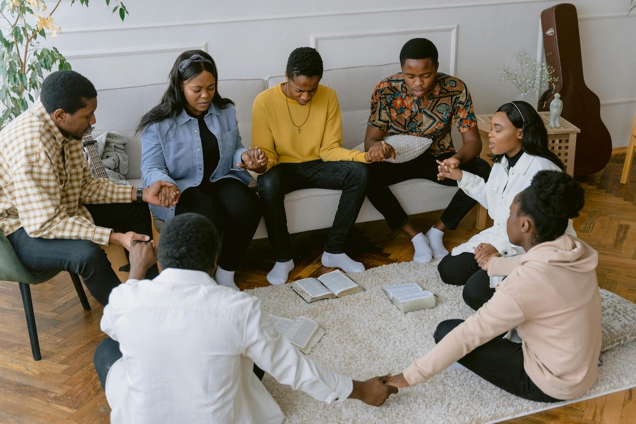 People sitting in a circle, holding hands while praying.
