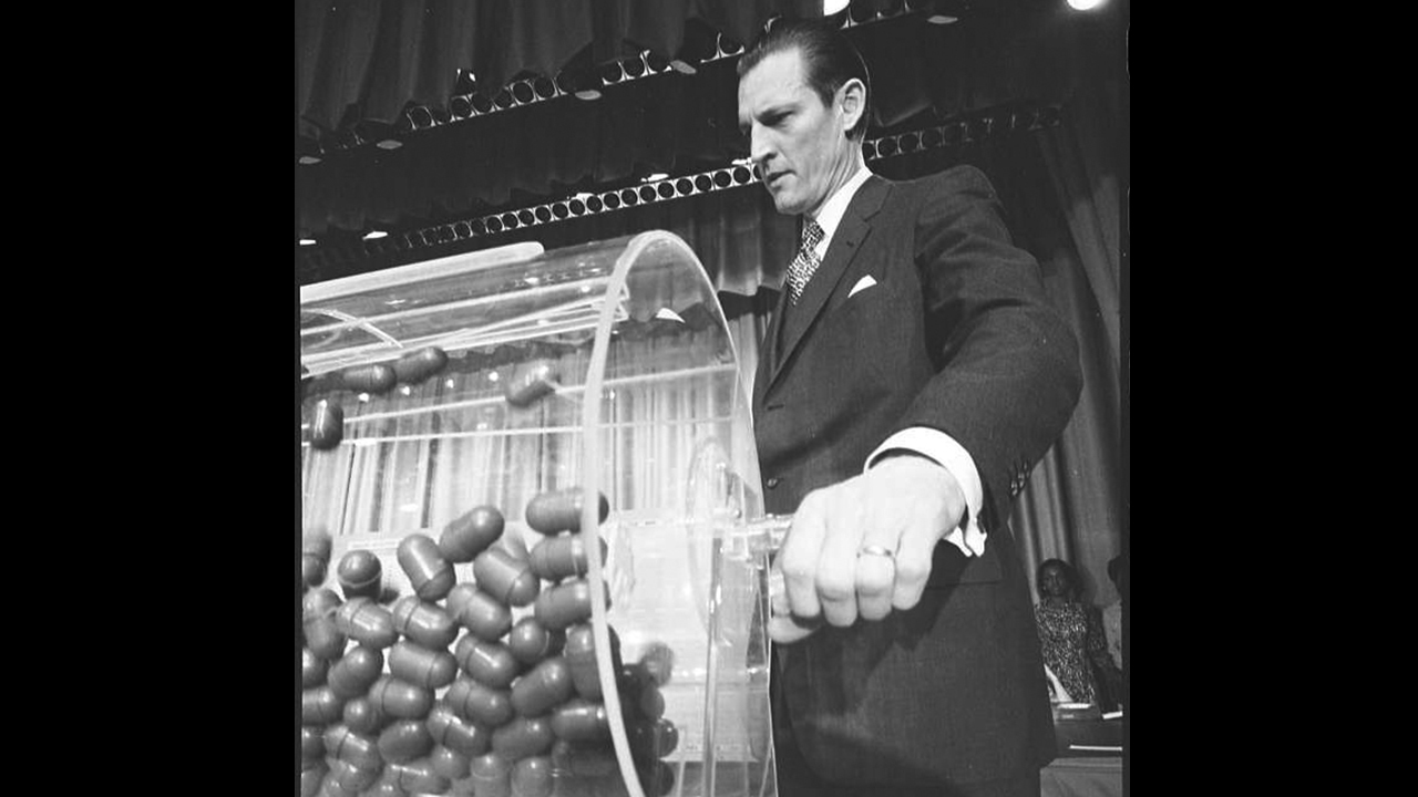 Selective Service System director Curtis W. Tarr turns the drum containing draft numbers Feb. 2, 1972 at the annual draft lottery. — Thomas J. O’Halloran/Library of Congress/Picryl
