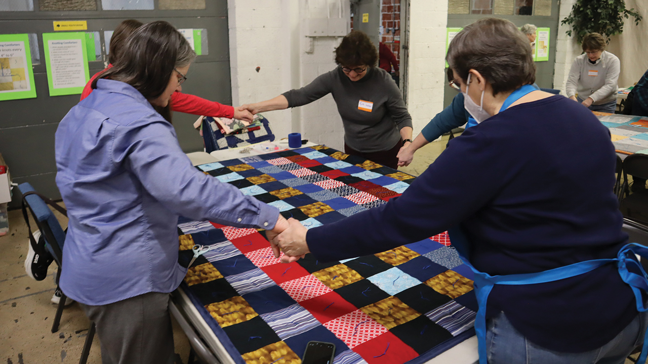 Volunteers at Harrisburg Brethren in Christ Church pray for the person who will receive the comforter they’ve completed. — Laura Pauls Thomas/MCC