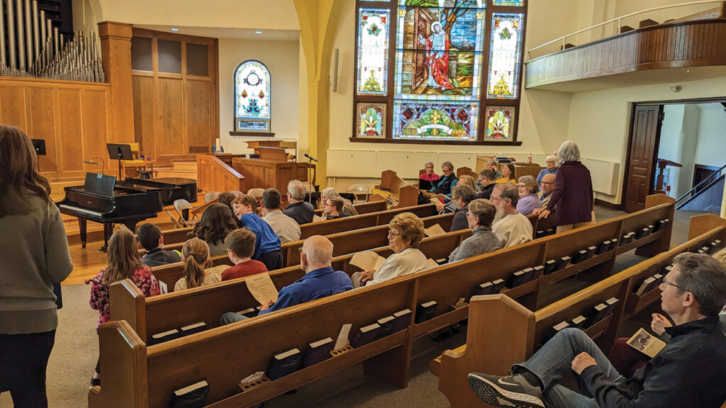 Beneath a window depicting Jesus knocking at the door, people gather at First Mennonite Church in Bluffton, Ohio. — Courtesy of Phil Yoder