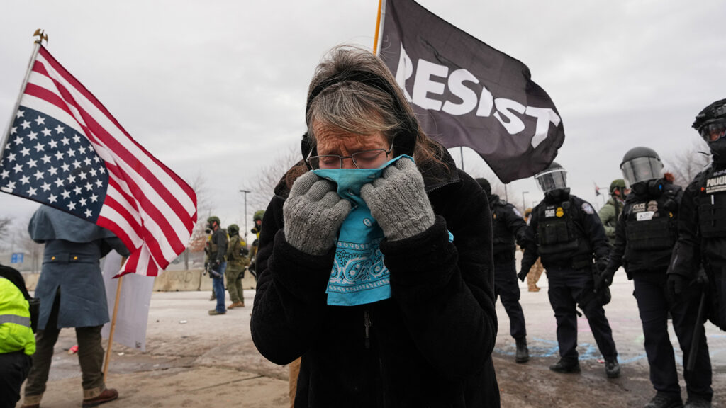 A woman covers her face from tear gas as federal immigration officers confront protesters Jan. 15 in Minneapolis. An upside-down U.S. flag signals distress. — Adam Gray/AP
