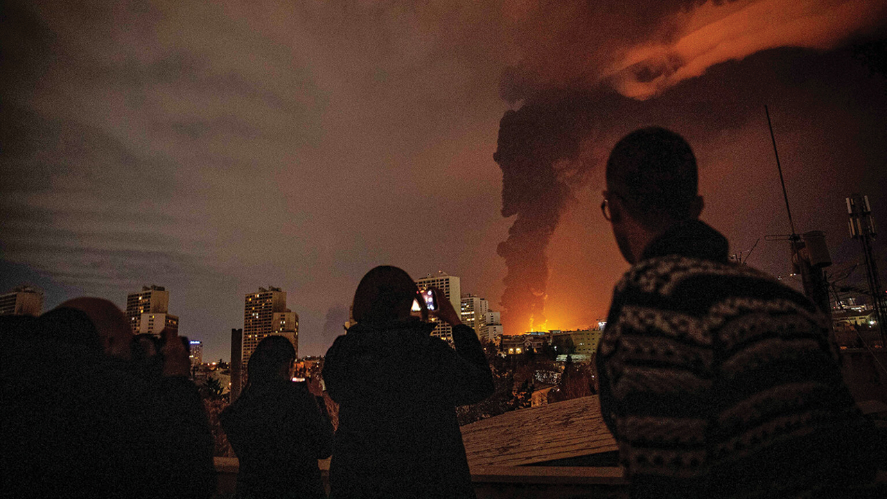 Residents look on as flames and smoke rise from an oil storage facility struck as attacks hit the city during the U.S.–Israeli military campaign in Tehran, Iran, March 7. — Alireza Sotakbar/ISNA via AP