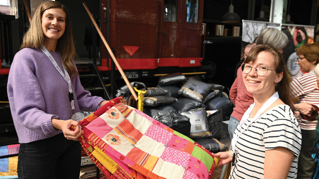 Eileen Hofer, left, and Melanie Rediger of Swiss Mennonite Mission Urgent Aid hold one of the comforters destined for Ukraine. — Scott Stoner-Eby/MCC
