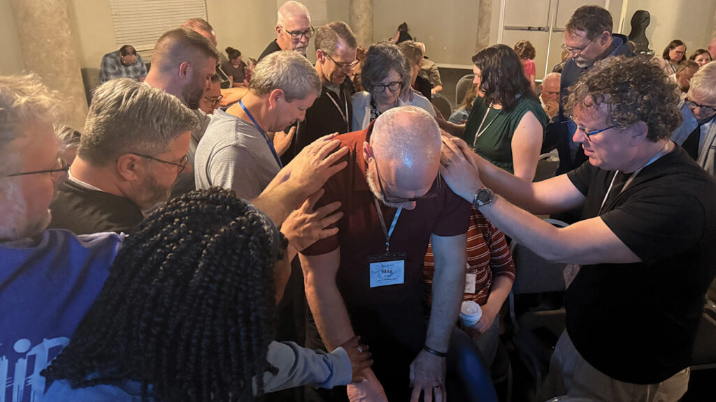 Evana members pray over Mike Hiebert, pastor of West Zion Mennonite Church, Moundridge, Kan., at a Flourish Retreat in February. — Evana Network