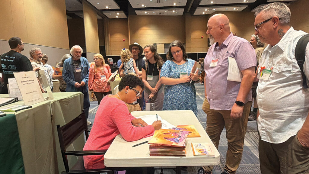 Gimbiya Kettering signs copies of her new children’s book, Washing My Sister’s Feet, at the Church of the Brethren Annual Conference in Fort Wayne, Ind., in July. — Courtesy of Gimbiya Kettering