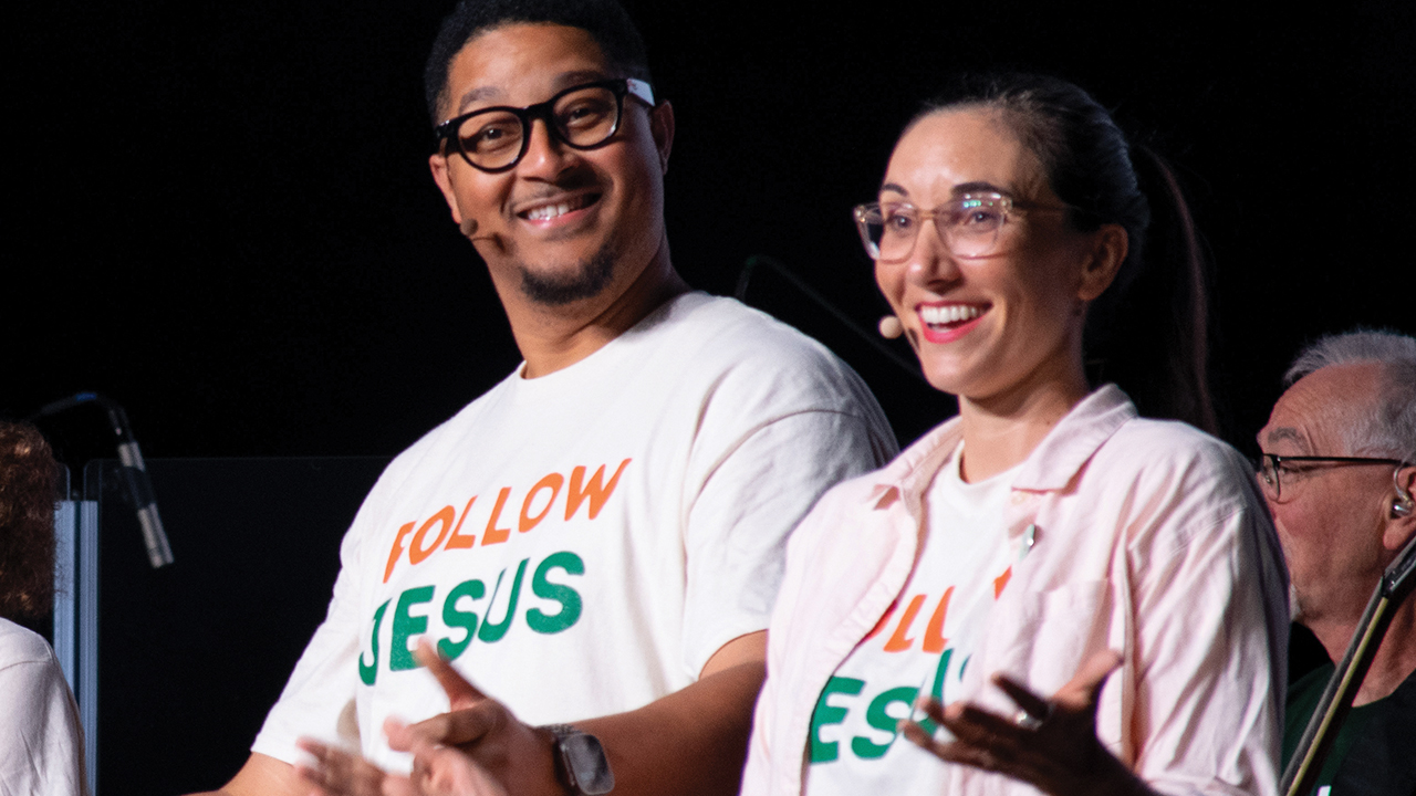FOLLOWING JESUS TOGETHER: Pastors Caleb McClendon of Hampton, Va., and Melissa Florer-Bixler of Raleigh, N.C., greet the crowd at the 2025 Mennonite Church USA convention in Greensboro, N.C. — Mackenzie Miller for AW